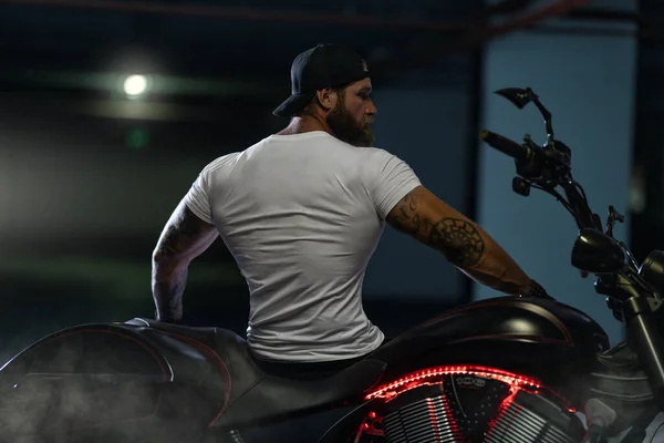 Seksi, yakışıklı, çekici, kaslı spor spor spor spor mankeni, park yerinde vahşi, güzel motosikletli, sırtı çerçeveli bir motosikletle poz veren bir motosikletli.
