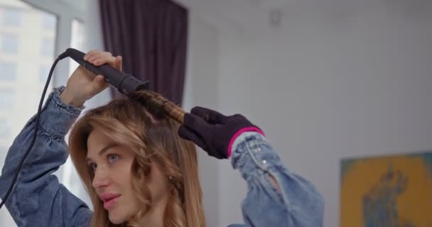 Wanita Muda Pirang Yang Cantik Memelintir Rambutnya Dengan Keriting Besi — Stok Video