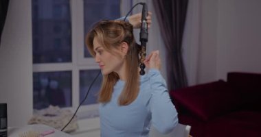 Mavi uzun kollu güzel mavi gözlü kız pencerenin kenarındaki buklelerini şekillendiriyor.