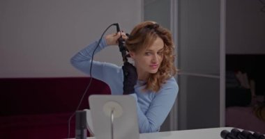 Güzel bir kız evinde özel bir bağlılığı olan saç maşasıyla kaotik kıvrımlar yapar.