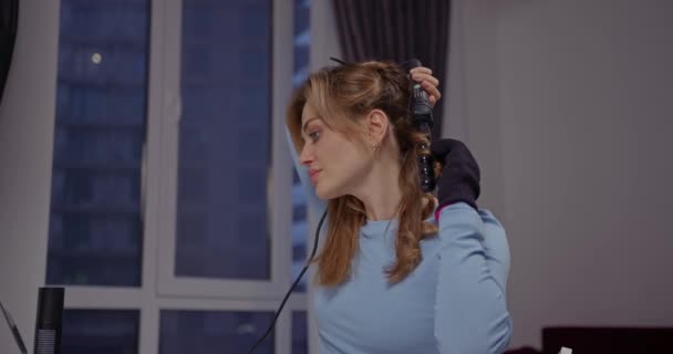 Молода Дівчина Красуня Блогер Завиває Волосся Завитковим Залізом Біля Вікна — стокове відео