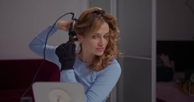 Tombul dudakları olan çekici bir kız saçını saç maşasıyla şekillendiriyor..