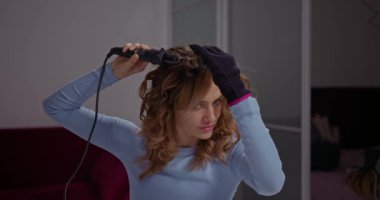 Güzel kız elinde koruyucu eldivenle kızgın bir saç maşasıyla kıvırcık yapıyor..