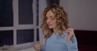 Genç, güzel, sarışın kız yeni stil kıvırcıklarını eliyle düzeltiyor.