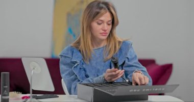 Güzel sarışın bir kız saçlarını kıvırcık saçlarıyla yapmak üzere ve büyük siyah kutudan saç maşasını çıkarıyor. Kot ceketli hoş bir kadın evde buklelerini yapacak.