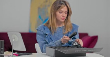 Güzel sarışın bir kız saçlarını kıvırcık saçlarıyla yapmak üzere ve büyük siyah kutudan saç maşasını çıkarıyor. Kot ceketli hoş bir kadın evde buklelerini yapacak.