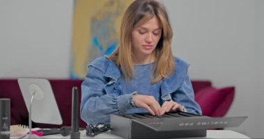 Güzel sarışın bir kız masadaki küçük bir aynanın önünde saçını tarıyor. Kot ceketli hoş bir genç kadın saçını pembe bir tarakla tarıyor.