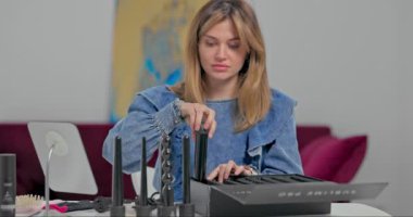 Güzel sarışın bir kız masadaki küçük bir aynanın önünde saçını tarıyor. Kot ceketli hoş bir genç kadın saçını pembe bir tarakla tarıyor.