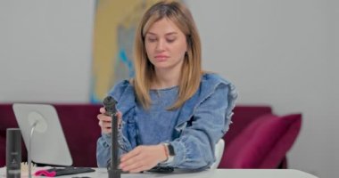 Masadaki mavi gözlü sarışın genç kadın saç stili dersi vermeye hazırlanıyor, saç maşasına bağlanıyor.