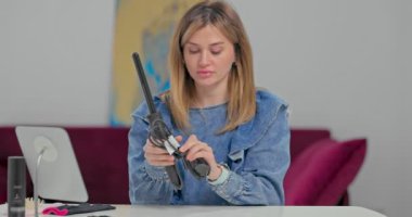 Mavi gözlü sarışın genç kadın saç masanda otururken saç maşasını çözer ve saçını yapmaya hazırlanır.