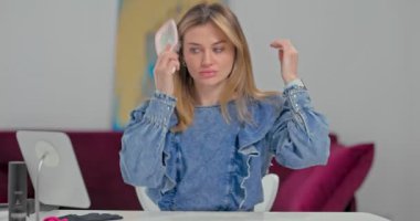 Sarışın genç bir kadın aynanın önünde otururken saçını tarar, kendini saç maşasından korumak için kalın bir eldiven giyer.