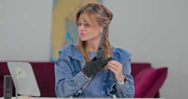 Güzel sarışın genç kadın saçını saç maşasıyla kıvırıyor, neşeli saçlar bukleleri çalıyor, mükemmel bukleler yaratma üzerine özel ders veriyor.