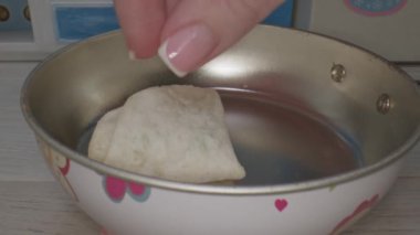 Küçük bir mutfakta, minyatür bir yemek ortamında, küçük bir tabağa baharatlı bir el serpintisi serpiştiriyor. Sahne küçük yemek takımlarının detaylarını vurguluyor.