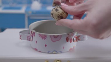 Küçük bir tencereye benekli bıldırcın yumurtasını nazikçe yerleştiriyor. Yemek pişirme gösterisinin bir parçası olarak karmaşık detayların altını çiziyor..