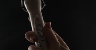 Siyah arka planda bir kadın eli tarafından dalgalı saç yapmak için profesyonel bir saç maşasının göstergesi.