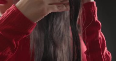 Kırmızı elbiseli esmer kadın parmaklarını dalgalı saçlarında gezdirip izole edilmiş siyah arka planda hipnotize edici bir etki yaratıyor.
