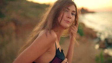 Güzel, uzun boylu bir kız güneşin doğuşunda sakin bir kumsalda duruyor. Hafif bir esinti ve güneşin sıcaklığını hissediyor. Huzurlu bir sabahı kucaklayan saçlarını çalıyor.