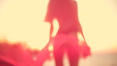 Güzel, uzun boylu bir kız gün doğumunda sahilde dalgalı bir atkı tutuyor. Şafağın ılık renkleri siluetini nazik dalgalara sarıyor. Huzurlu bir atmosfer yaratıyor.