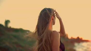 Uzun boylu kız kumsalda gün doğumunda uzun saçları rüzgarda savrulurken şafağın ufuk renklerine bakarken yansıma anı için sakin bir zemin oluşturur.