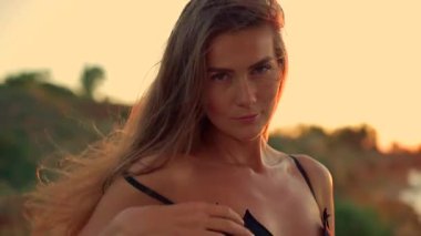 Güzel, uzun boylu bir kız gün doğumunda sahilde duruyor. Yumuşak güneş ışığı onun özelliklerini aydınlatıyor ve sakin atmosfer dalgaları oluşturuyor. Okyanus dalgaları yavaşça kıyıya vuruyor.