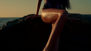 Güzel uzun kız gün doğarken kayalık sahilde oturur ve tenini öper. Sabahın erken saatlerinde huzur içinde dalgalar yavaşça kıyıya vurur.