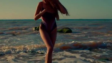 Uzun boylu kız zarif bir şekilde sahilde duruyor. Silüeti gündoğumunun sıcak renklerine vurgu yapıyor. Hafif dalgalar, sakin sabahı kucaklarken ayaklarını öpüyor.