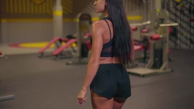 Jimnastik salonunda kız, elinde pembe karıştırıcıyla güvenle yürür. Spor için uygun siyah bir kıyafet giymişti..