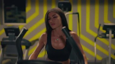 Kız Stepper 'ın çağdaş spor salonu parlak sarı dekorunda kardiyo çalışması yapıyor. Düzenli tempoyu korurken egzersiz rutinine odaklanıyor..