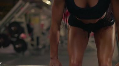 Kız spor salonunda halter kullanarak ağırlık kaldırma hareketlerine odaklanıyor. Gücünü ve adanmışlığını gösteriyor. Formda ve güçte egzersiz yaparak spor yapma hedeflerini vurguluyor.