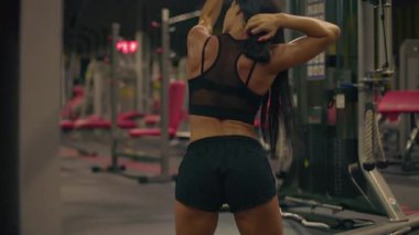 Kız üst çapraz sorgulama yapıyor göbeğine odaklanıyor ve iyi donanımlı spor salonunda kararlılığını gösteriyor. arkaplanda çeşitli çalışma makineleri ve ekipmanlar var.