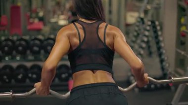Kız sırt kaslarını hedef alarak ters tutuş halteri sırasına giriyor ve iyi donanımlı spor salonunu hedef alıyor. Antrenman sırasında formuna odaklanıyor..