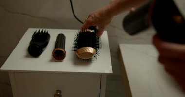 Çağdaş bir banyoda kadın elleri, dingin bir ortamda kişisel bakım rutinini gösteren saç kurutma makinesine çeşitli hortumlar bağlamaya odaklanır..