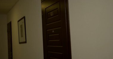 Güzel sarışın kadın ön kapıyı açar ve dışarı, aydınlık bir koridora adım atar. Ayar, modern görünümü artıran temiz çizgiler ve asgari dekor içeriyor..