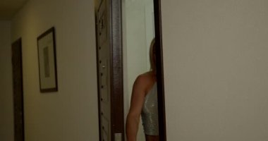 Güzel sarışın kadın ön kapıyı açar ve güneş ışığına doğru yürür. Kendine güveni ve neşeli tavırlarıyla günü kucaklamaya hazır görünüyor..