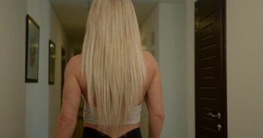 Güzel sarışın kadın zarif bir şekilde aydınlık bir koridorda yürüyor. Sonunda yüzünü kameraya çeviriyor uzun saçlarını gösteriyor ve o anı yakalayan parlak bir gülümseme..