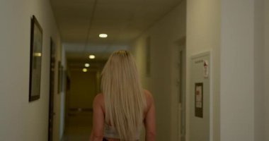 İyi aydınlatılmış bir koridorda güzel bir sarışın kadın saçlarından aşağı doğru süzülüyor. Çekici bir gülümseme ile kameraya döner kendine güven ve cazibe saçar..