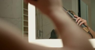 Şık bir banyoda kadınlar saç kurutma makinesini ustalıkla kullanır eşsiz bir eklenti bukleler ve permalar yaratır. O, yansımasını kontrol ederken saçına odaklanıyor..