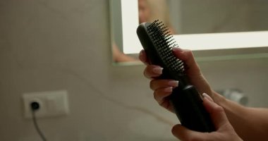Çağdaş bir banyoda kadın elleri saç kurutma makinesine hortum bağlamakla meşguldür. Hazırlıklar, kuaförlük, kuaförlük, kuaförlük gibi konulara odaklandığını gösteriyor..