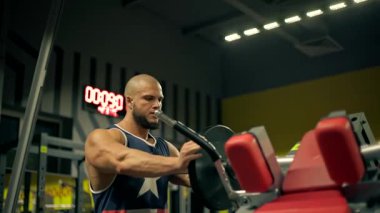 Kel sporcu sakalı spor salonunda bacak egzersizleri yapmaya odaklanıyor. Atmosfer enerjik bir şekilde sabah sporu boyunca kendini adamış ve güçlü olduğunu gösteriyor. makineye ağırlık yükler