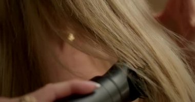 Parlak banyoda sarışın kız aynanın önünde dururken saç kurutma makinesi kullanıyor. Duştan sonra düzgün kilitlere odaklanır..