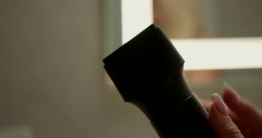 Eller, parlak bir banyodaki saç kurutma makinesine dikkatlice hortumlar takar. Rahatlatıcı atmosfer, kuaförlük için sabah hazırlığını vurguluyor.