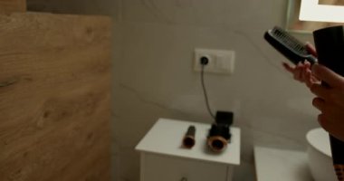 İyi aydınlatılmış bir banyoda biri sabah bakım seansına hazırlanırken çeşitli hortumları saç kurutma makinesine yerleştirir. Tezgahta bir saç fırçası ve diğer gerekli şeyler var..