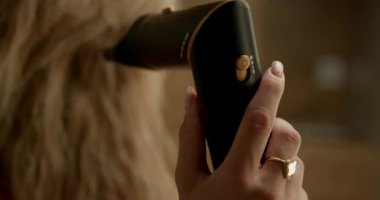 Sarışın bir kız aynanın önünde el kurutma makinesiyle saçını kurutuyor. Kilitlerinden sıcak hava akıyor. Onları dikkatlice şekillendiriyor. Kendine baktığı anı yakalıyor..