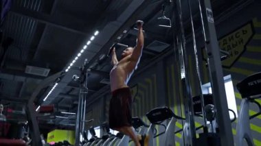 Kaslı adam iyi donanımlı bir spor salonunda barfiks çekiyor. Parlak spor salonu onun dayanıklılık eğitimine olan bağlılığını vurguluyor. Ekipman ve spor meraklıları etrafını sardı..