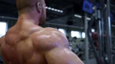 Kas yapısı olan bir adam modern bir spor salonunda ağırlık antrenmanı sırasında kendini adadığını gösterir. Çevre, spor aletleri ile donatılmıştır..