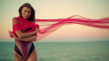 Şafak vakti kumsalda zarif bir şekilde duran uzun boylu kız eşsiz bir mayo giyiyor ve büyüleyici bir atmosfer yaratıyor.