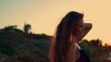 Sakin kumsalda gün doğumunda uzun boylu kız zarif bir şekilde ayakta duruyor. Uzun saçları yumuşak ve dingin suları yakalıyor. Şafağın renklerini yansıtıyor. Huzurlu bir atmosfer yaratıyor.