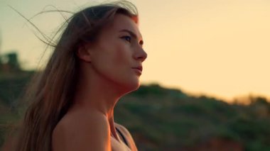 Uzun boylu kız kumsalda gün doğumunda saçlarını hafifçe savurarak ufuk çizgisine bakıyor. Sabah ışıklarının ve sakin dalgaların dingin güzelliğini kucaklıyor.