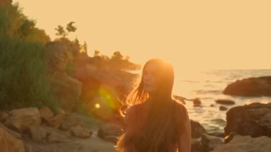 Güzel, uzun bir kız sahilde duruyor güneş doğarken üzerine altın parıltı saçıyor ve okyanus dalgalarını aydınlatıyor sakin bir atmosfer huzurlu bir başlangıç günü sunuyor