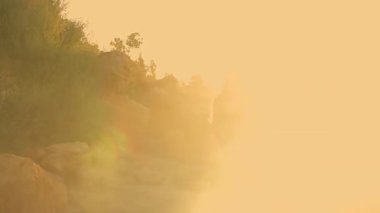 Uzun kız kumlu kumsalda duruyor güneş doğuyor. Erken ışığın yumuşak parıltısını kucaklıyor. Sakin dalgalar, ufuk çizgisine bakarken ayaklarını hafifçe vuruyor.